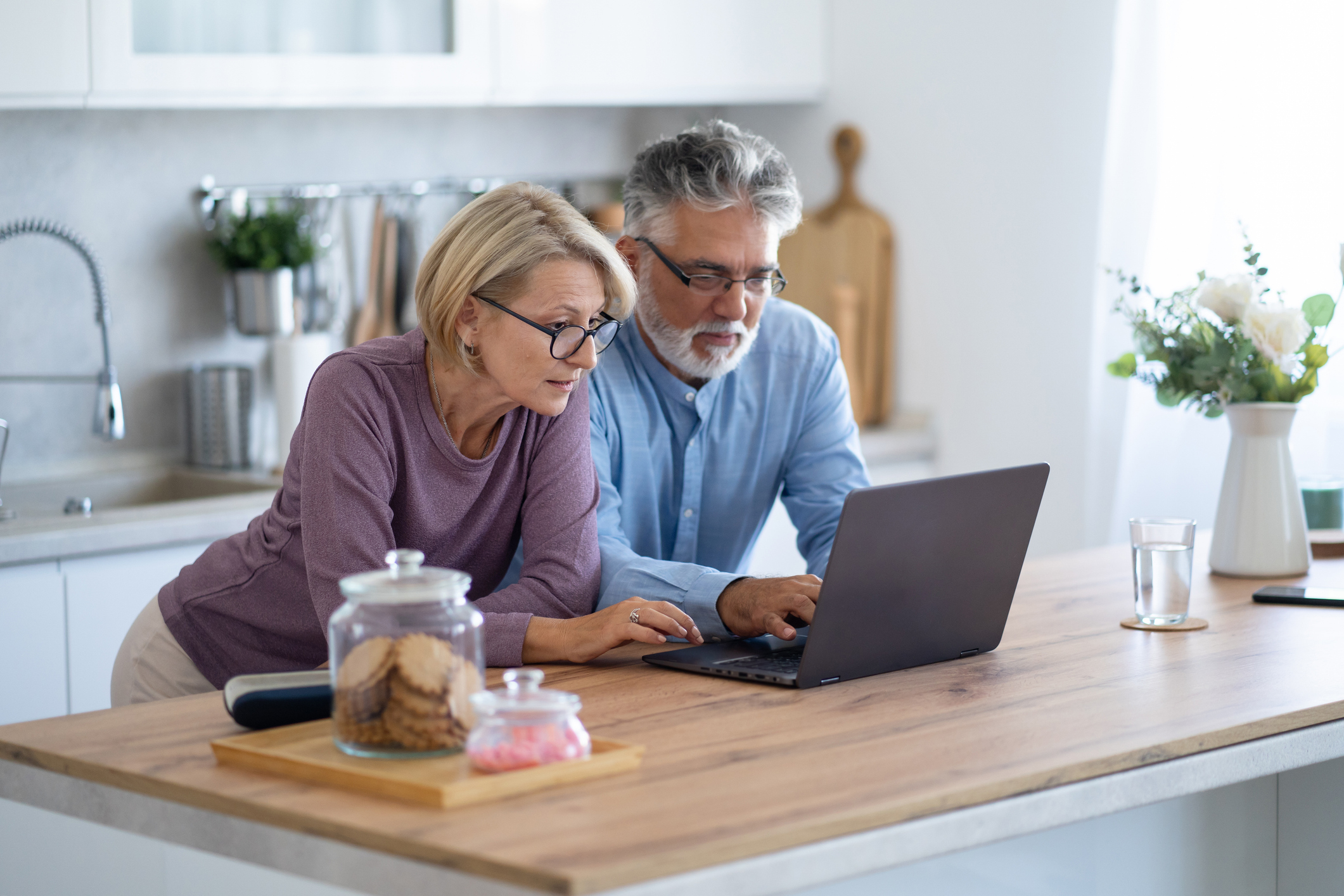 Learning the laptop together A senior couple are leaning next to each other, both touching a laptop keyboard as they help each other navigate the online world